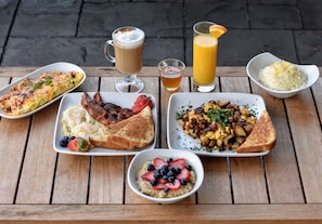 A wooden table with breakfast items including toast, eggs, bacon, and a bowl of fruit.
