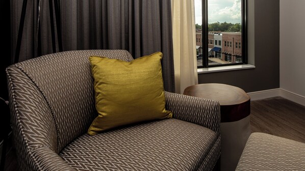 Una habitación con un sillón estampado, una mesita de madera redonda y vistas a edificios a través de una ventana.