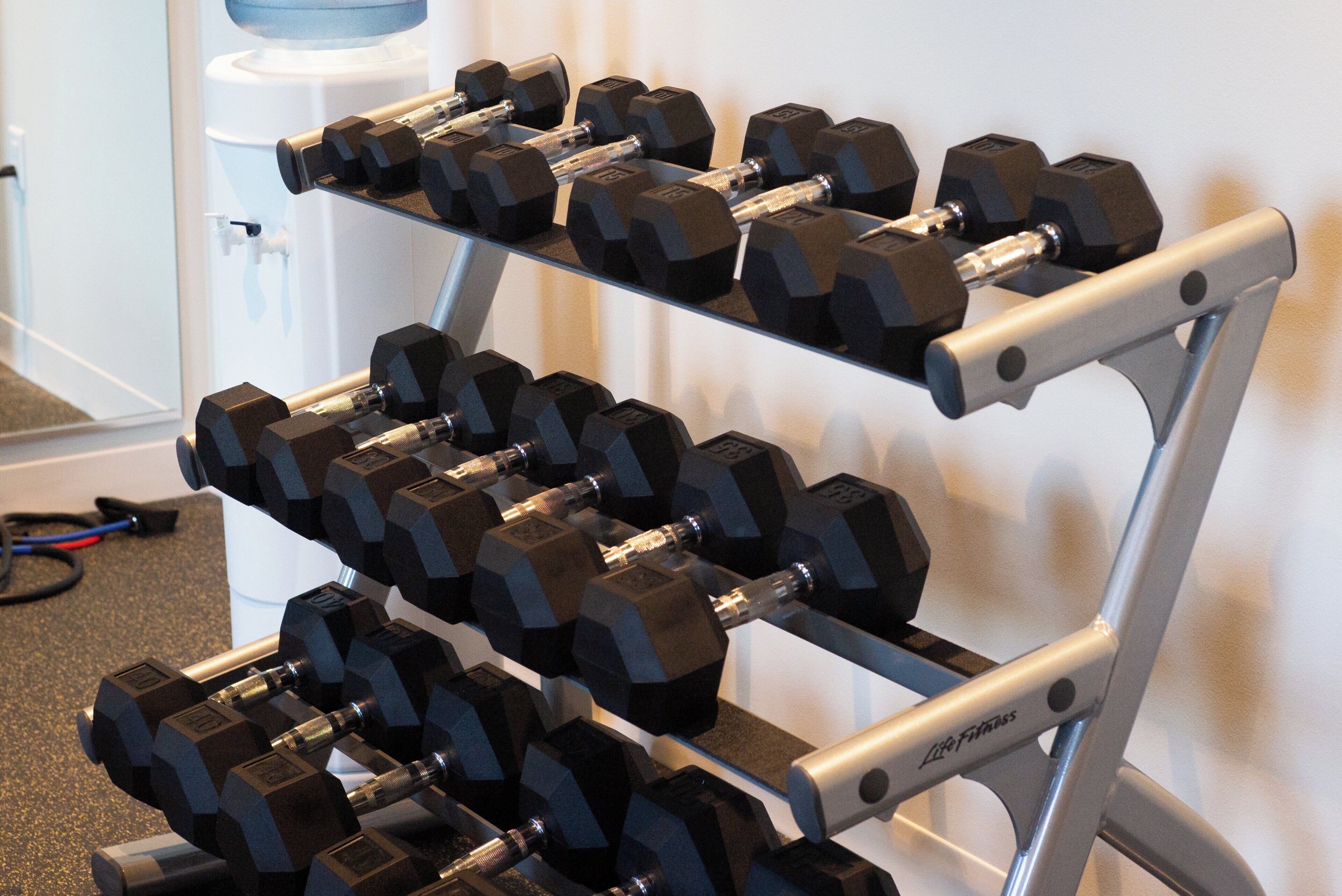 A rack of black dumbbells with weight markings, a water dispenser, and a white wall.