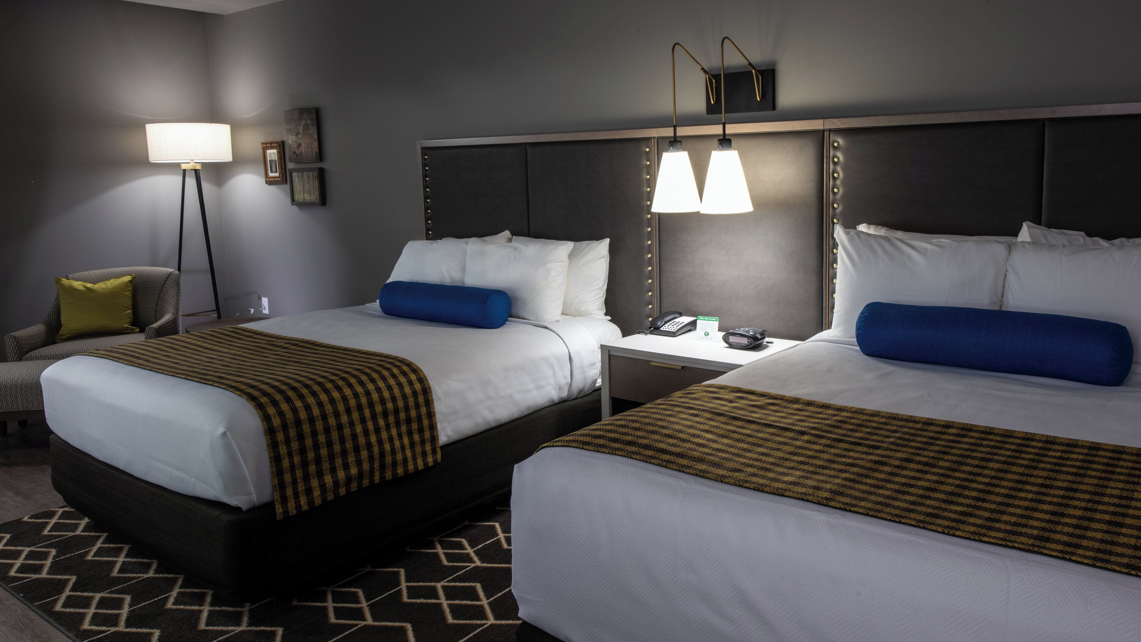 Habitación de hotel con dos camas, una mesita de noche, una lámpara y un teléfono fijo en la pared.