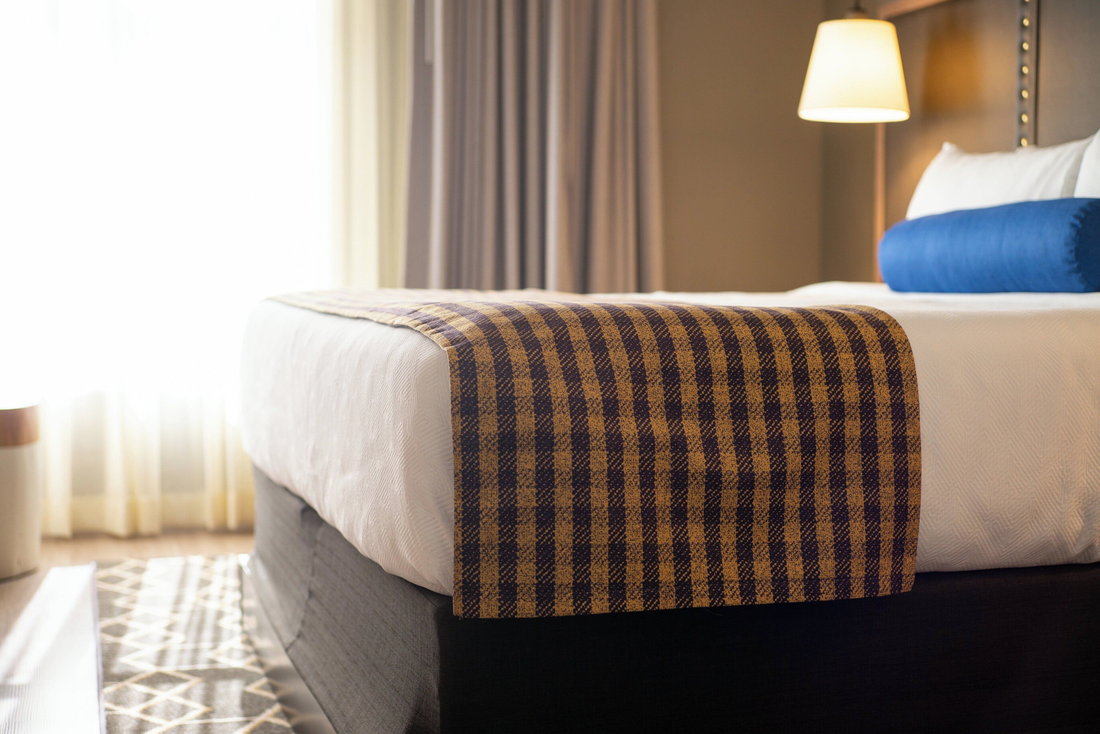 Un lit bien fait, avec une couverture à motifs, un oreiller et une lampe de chevet.