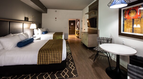A hotel room with two beds, a desk, a chair, a TV, and a small table.