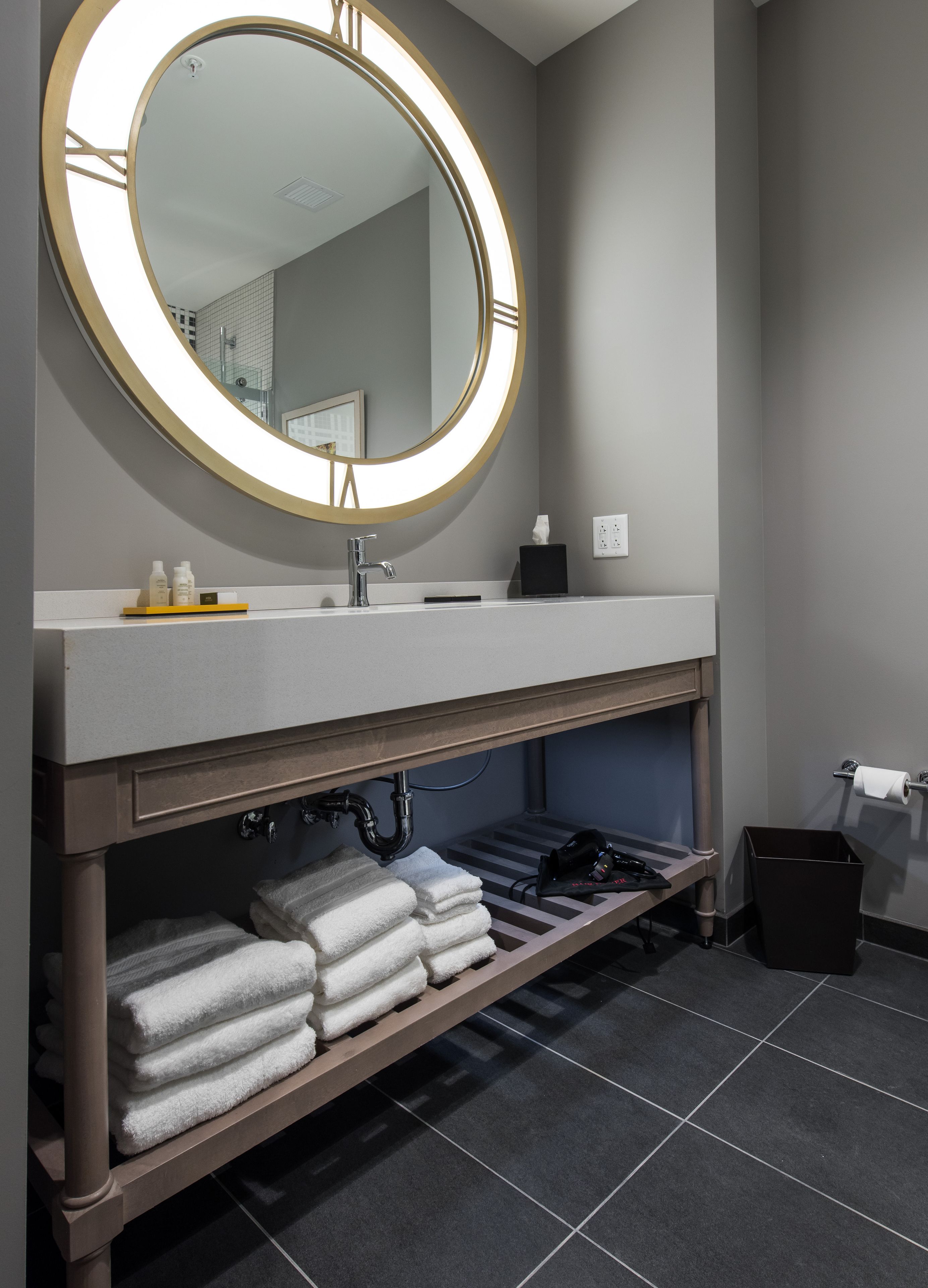 A modern bathroom with a round mirror, a sink, and a shelf with towels.