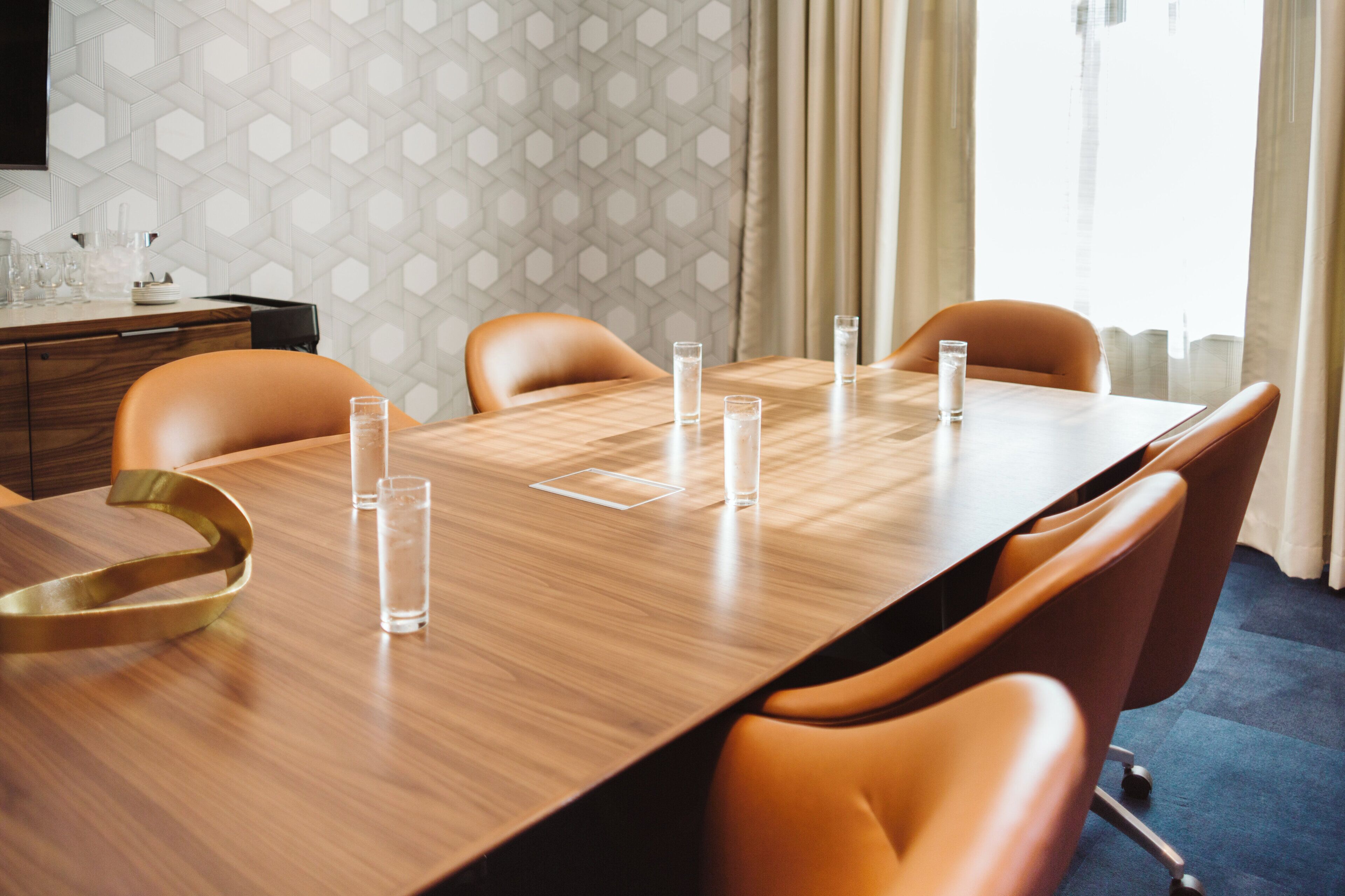 Een vergaderzaal met een lange tafel, zes stoelen en zes glasjes water.