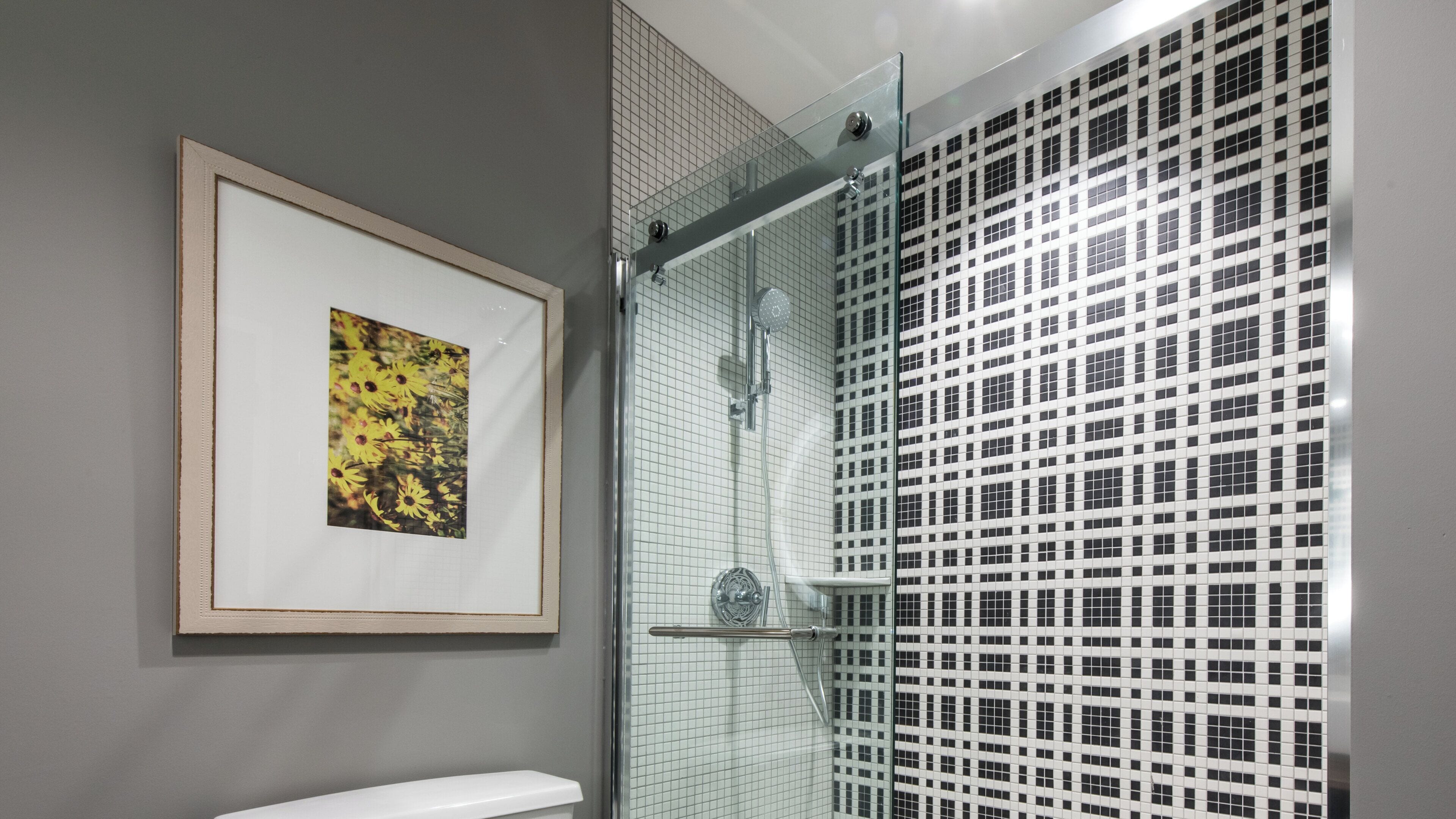 A bathroom with a glass shower enclosure, a framed picture on the wall, and a tiled shower wall.