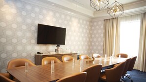 A conference room with a long table, multiple chairs, a flat-screen TV, a coffee machine, and a window with curtains. - Hotel Indigo Hattiesburg by IHG (Hattiesburg)