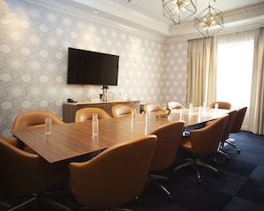 A conference room with a long table, multiple chairs, a flat-screen TV, a coffee machine, and a window with curtains. - Hotel Indigo Hattiesburg by IHG (Hattiesburg)