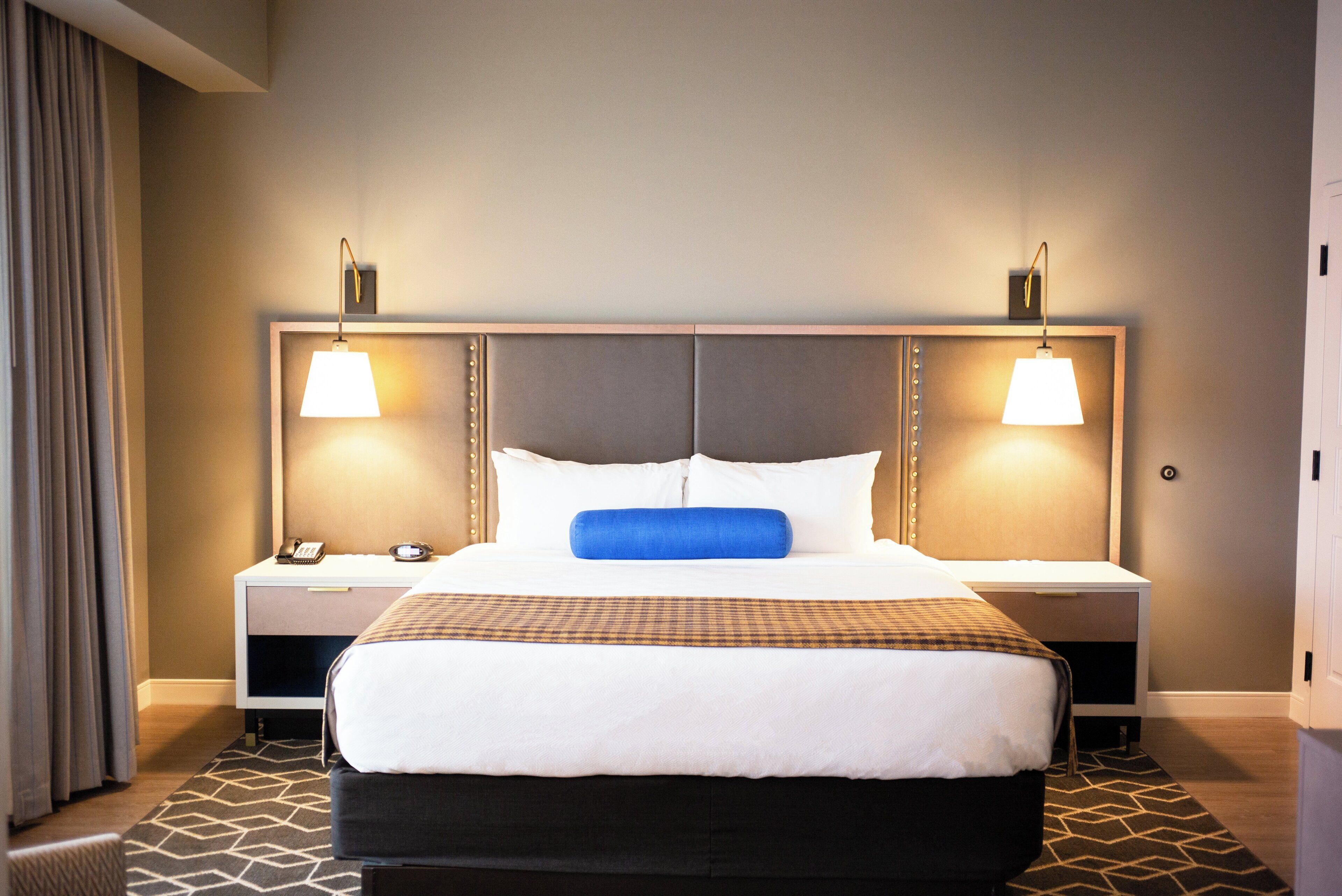 A hotel room with a large bed, two bedside tables, a nightstand with a telephone, and a wall-mounted lamp.