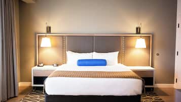 A hotel room with a large bed, two bedside tables, a nightstand with a telephone, and a wall-mounted lamp.