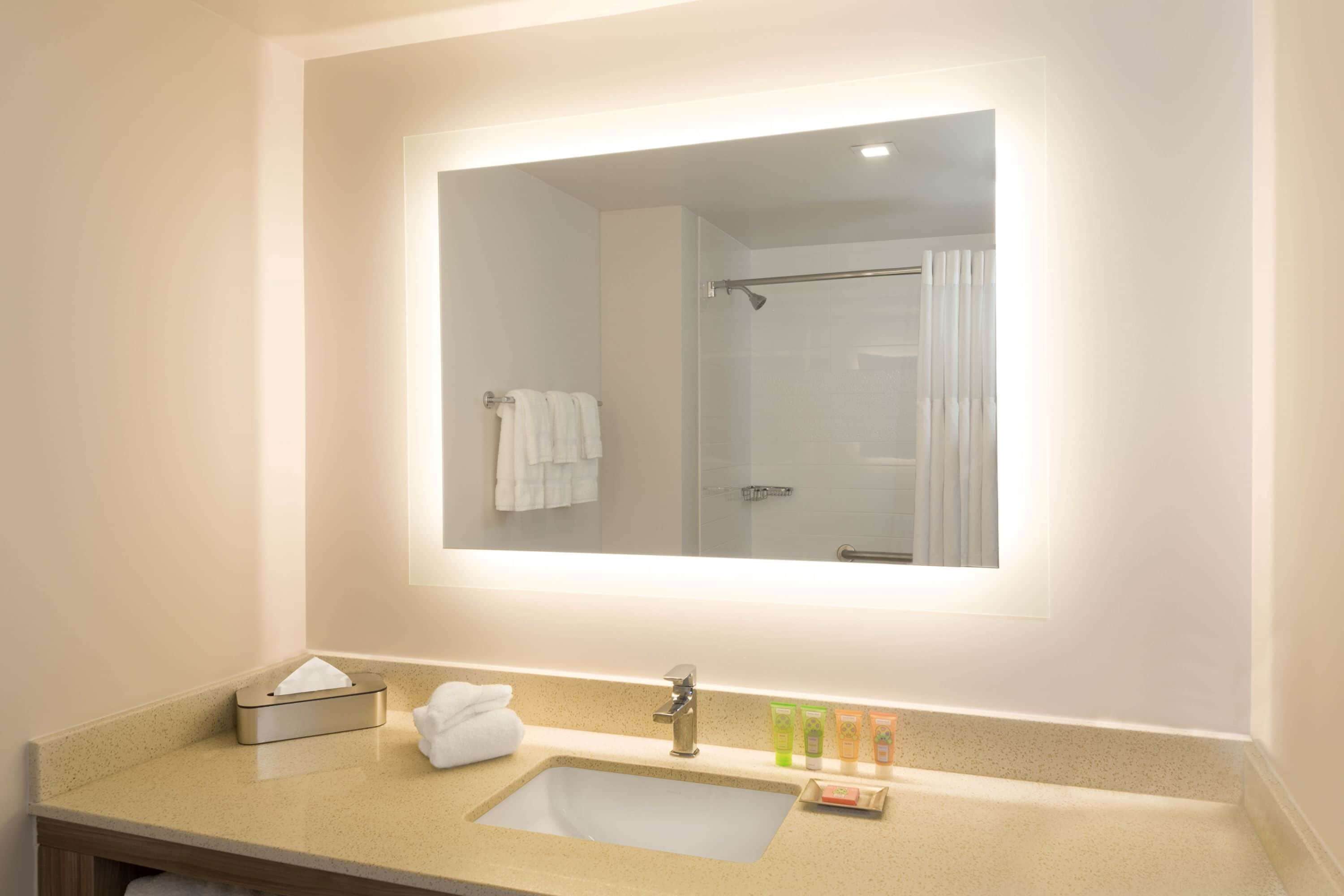 Un baño con lavamanos, espejo y artículos de aseo.
