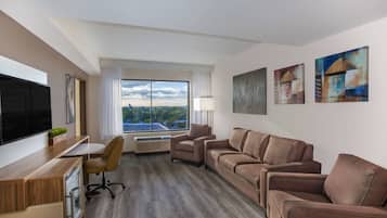 Quarto de hotel moderno com uma janela grande, TV de tela plana, escrivaninha, sofá e arte abstrata nas paredes.
