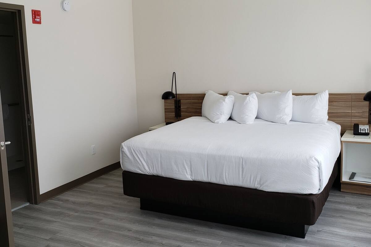 Habitación de hotel con cama, mesitas de noche, lámpara y detector de incendios.