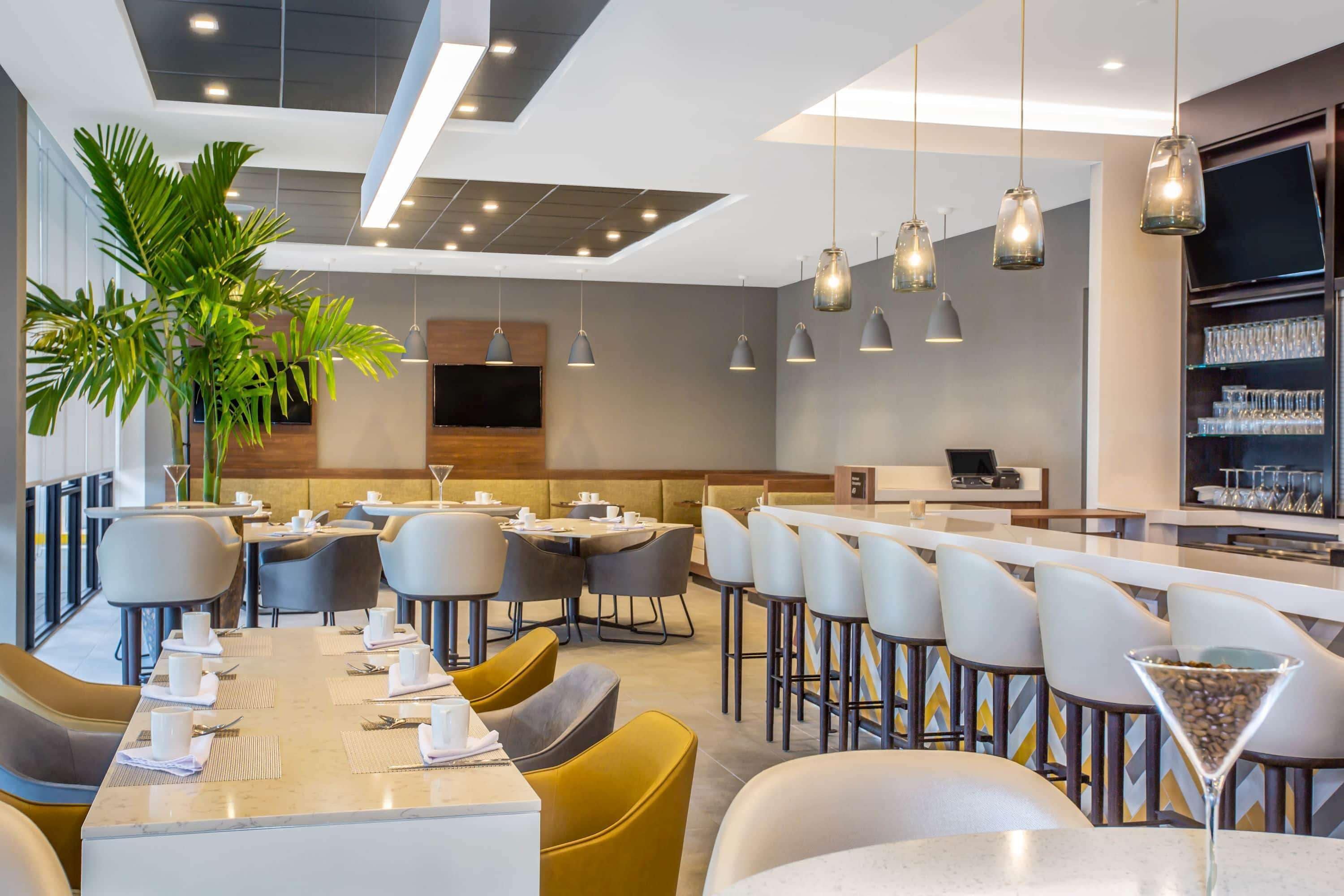 Un restaurante moderno con mesas altas, asientos de bar y una planta grande en maceta.
