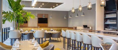 Un restaurante moderno con mesas altas, asientos de bar y una planta grande en maceta.