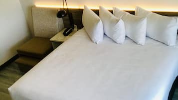 Una habitación de hotel con una cama grande, una mesita de noche con lámpara y un taburete pequeño.
