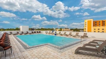 A rooftop pool with lounge chairs, a clear blue sky, and buildings in the background.