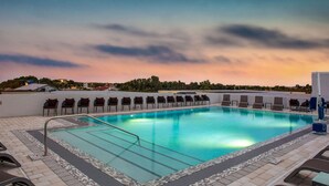 Piscina con sillones de descanso y vista al atardecer.