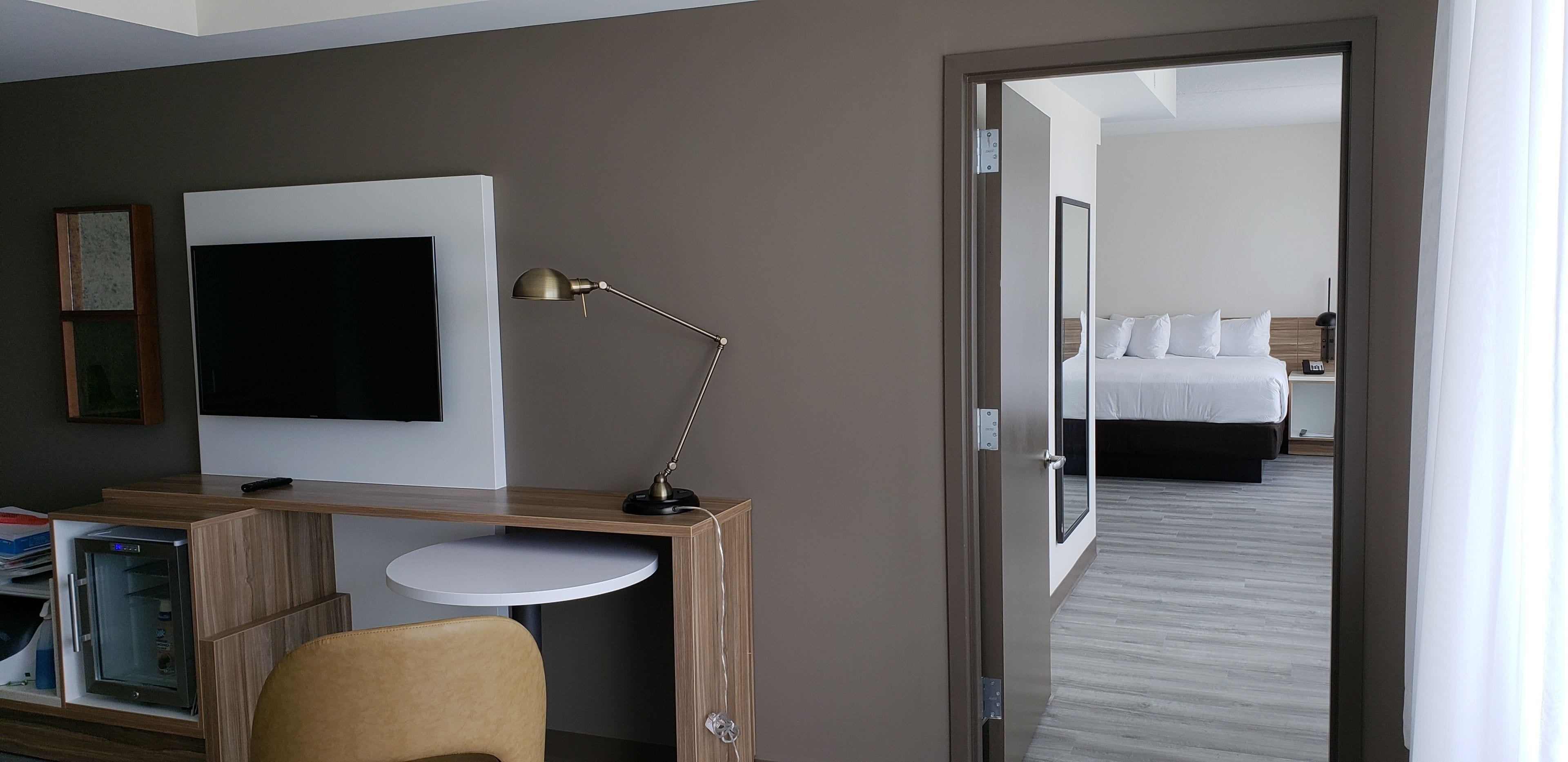 Une chambre d’hôtel équipée d’une télévision, d’un bureau, d’une chaise et d’un lit avec du linge de lit blanc.