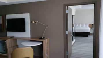 Une chambre d’hôtel équipée d’une télévision, d’un bureau, d’une chaise et d’un lit avec du linge de lit blanc.