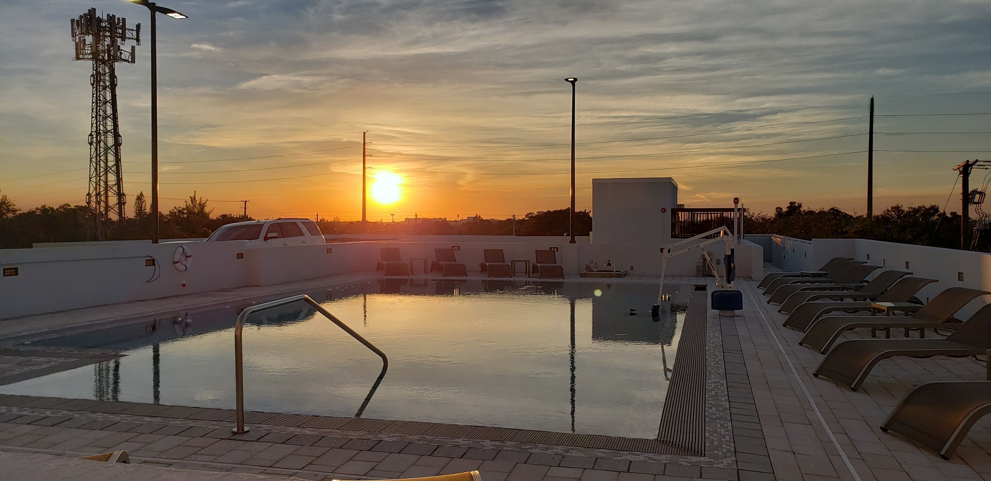 Piscina com cadeiras de descanso e pôr do sol ao fundo.