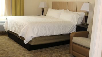 Une chambre d’hôtel avec un lit, deux tables de chevet avec des lampes, un fauteuil marron et un sol recouvert de moquette.