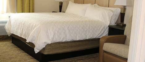 A hotel room with a bed, two bedside tables with lamps, a brown chair, and a carpeted floor.