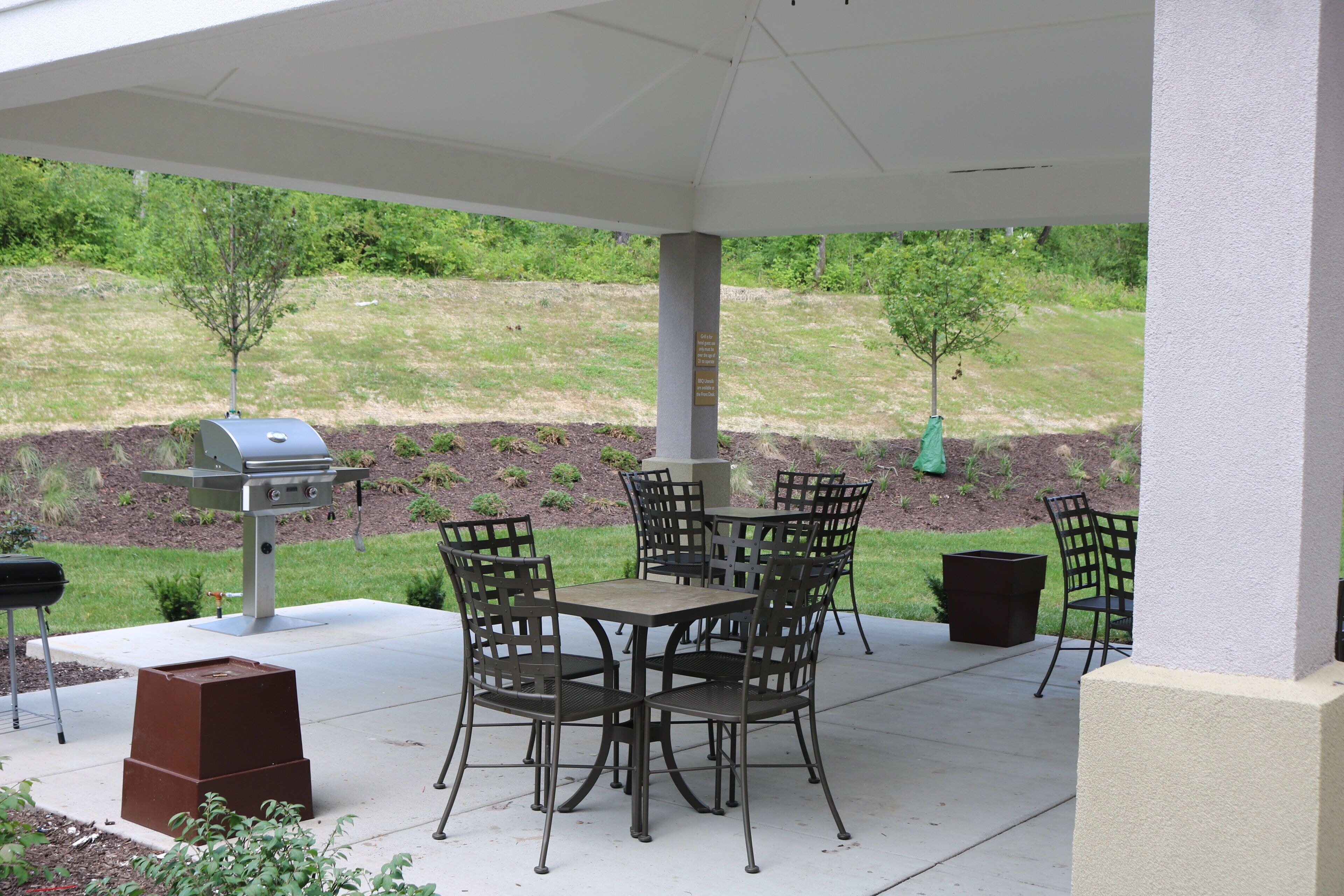 Un patio exterior con una parrilla, mesa y sillas.