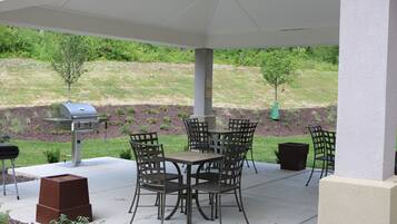 Un patio exterior con una parrilla, mesa y sillas.