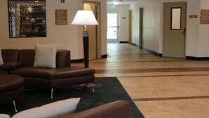 A hotel lobby with a brown leather sofa, a standing lamp, and a patterned rug. - Candlewood Suites Goodlettsville - Nashville by IHG (Goodlettsville)