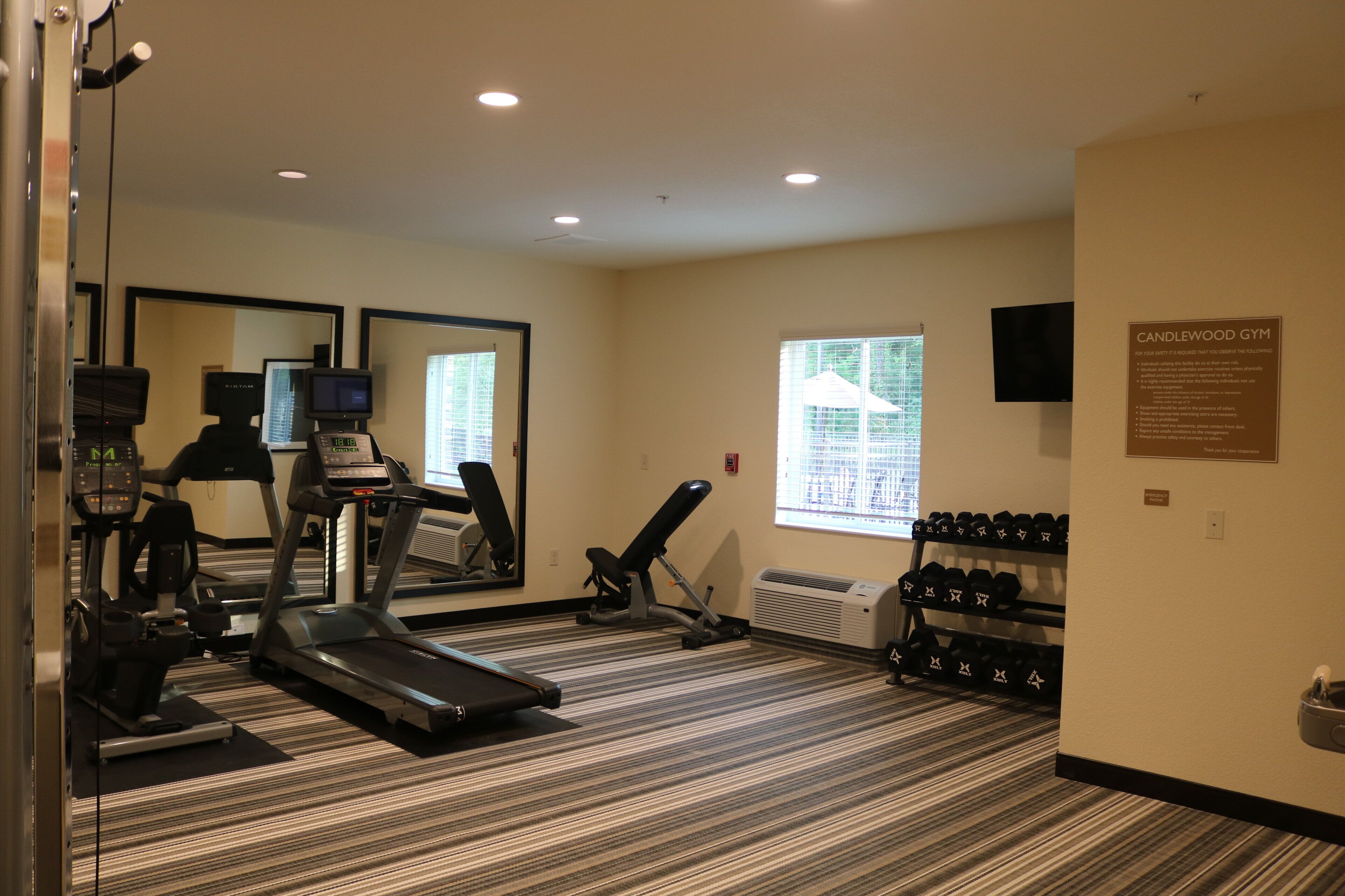 A gym with treadmills, a stationary bike, and a bench press. There is a mirror, a television, and a wall-mounted sign.