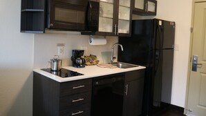 A compact kitchen with dark cabinetry, a black refrigerator, a microwave, and a coffee maker. - Candlewood Suites Goodlettsville - Nashville by IHG (Goodlettsville)