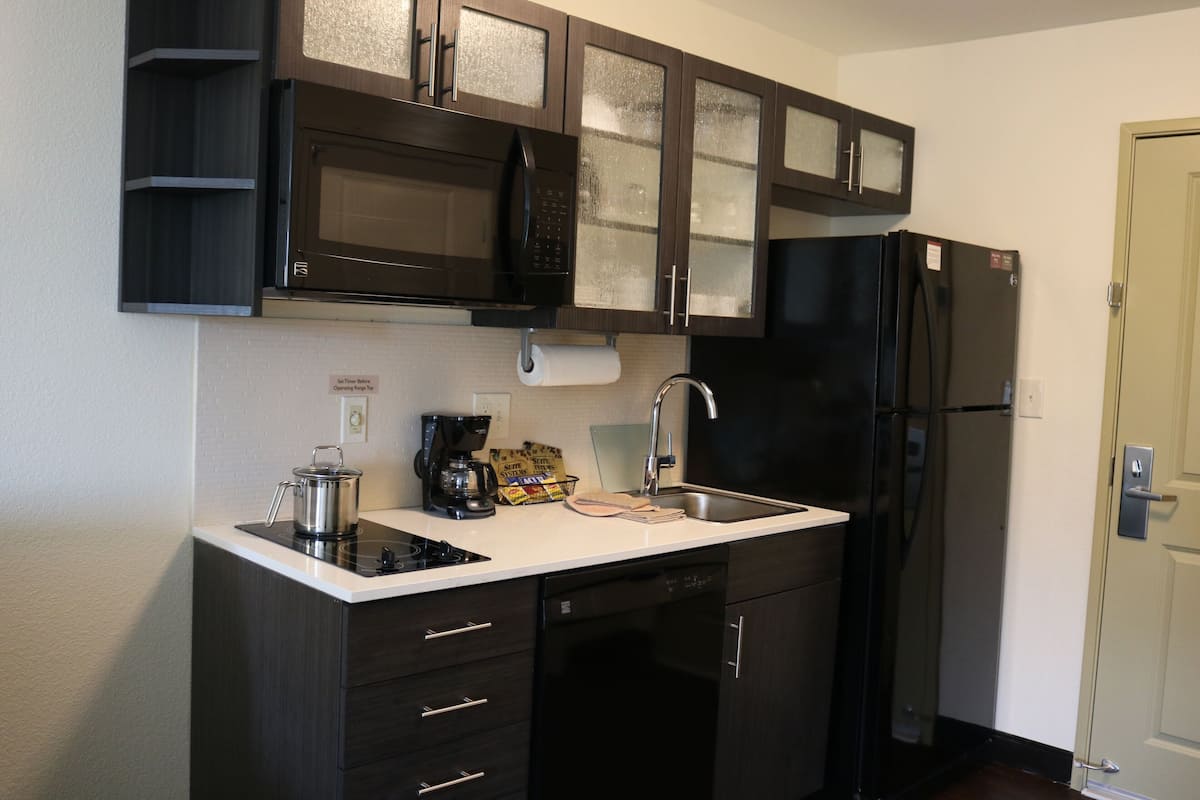 A compact kitchen with dark cabinetry, a black refrigerator, a microwave, and a coffee maker.