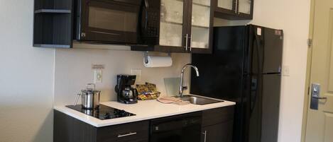 A compact kitchen with dark cabinetry, a black refrigerator, a microwave, and a coffee maker.