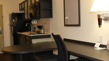 Ein Hotelzimmer mit Esstisch, Stühlen, einem Kühlschrank, einer Kaffeemaschine, einem Spiegel und einer Lampe.