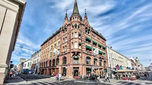 Een historisch gebouw met een opvallende toren en gebogen ramen, gelegen in een levendig stedelijk gebied met voetgangers en winkels.