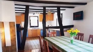 A dining area with a checkered tablecloth, wooden chairs, a vase with yellow flowers, and a wall-mounted TV displaying "NETFLIX". - Gräfrath Gästehaus Neunkirchen-Seelscheid (Neunkirchen-Seelscheid)