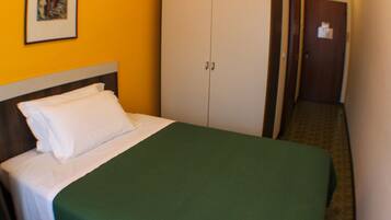 A hotel room with a bed, a green bedspread, white pillows, a wooden headboard, a white wardrobe, and a framed picture on the wall.