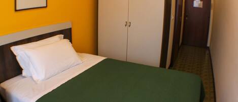 A hotel room with a bed, a green bedspread, white pillows, a wooden headboard, a white wardrobe, and a framed picture on the wall.