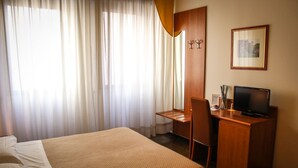 Een hotelkamer met een bed, een bureau, een stoel, een televisie en een ingelijste foto aan de muur.