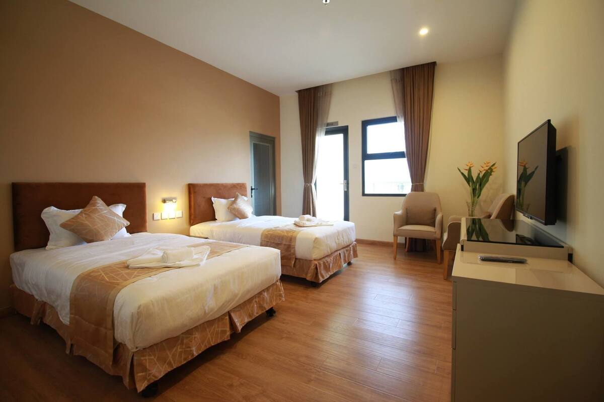 A hotel room with two beds, a desk, a chair, a TV, and a window with curtains.