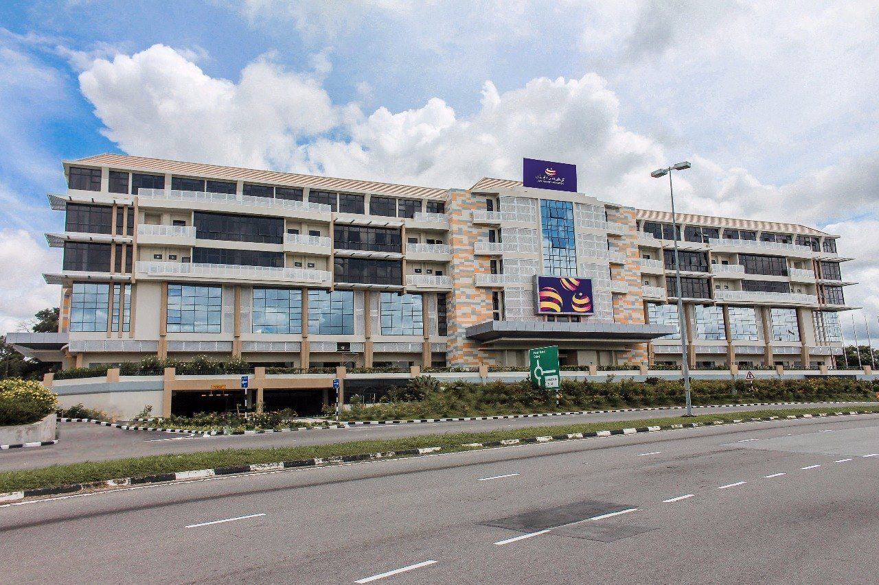 A multi-story hotel with a modern design, featuring a prominent logo on the facade and a clear sky in the background.