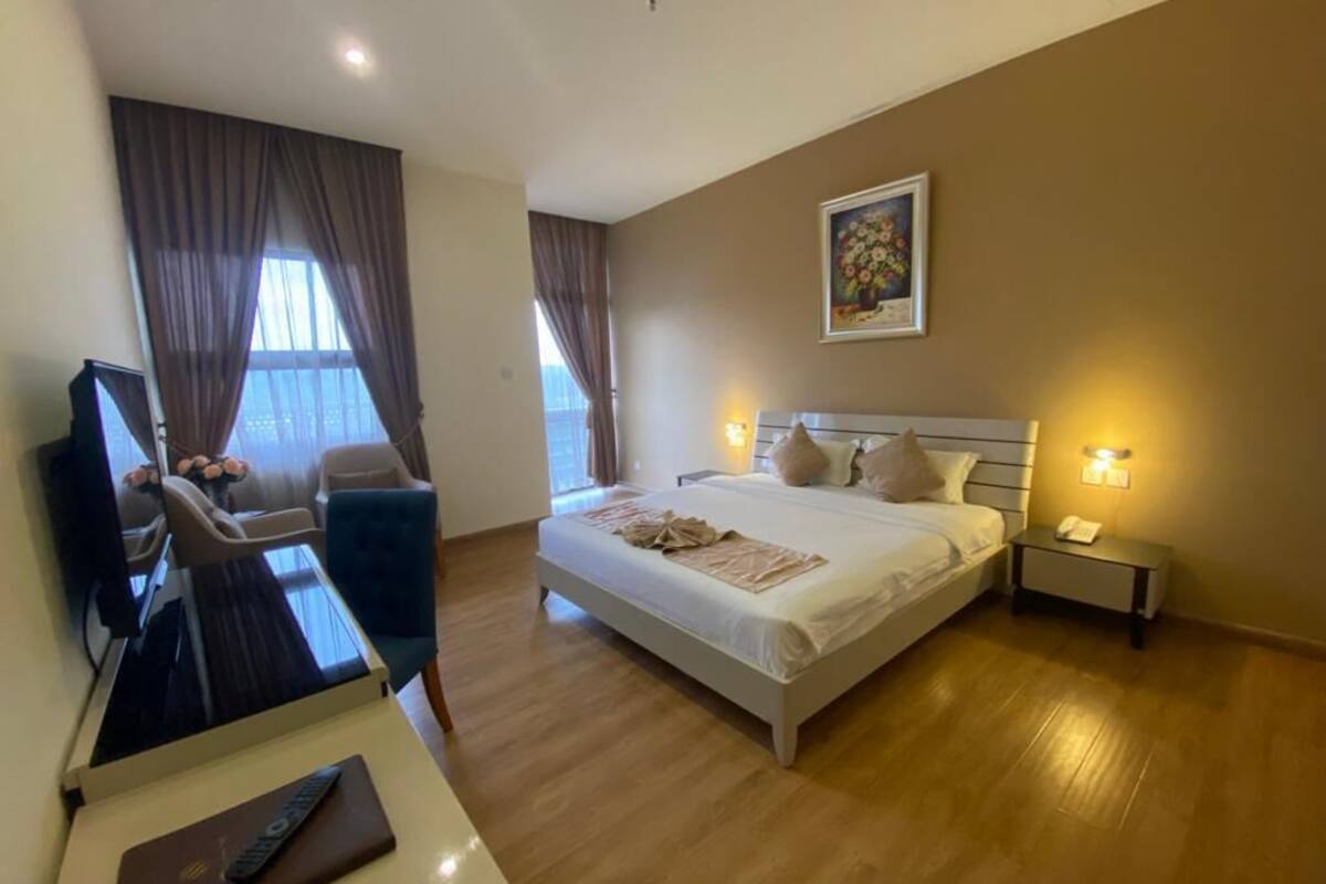 A hotel room with a bed, bedside tables, a desk with a chair, a television, and curtains.