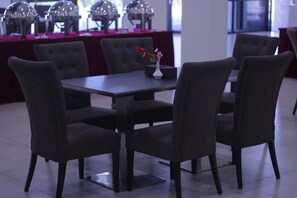 A dining area with a rectangular table, six upholstered chairs, and a vase with flowers on the table. - Wafa Hotel & Apartment (Bandar Seri Begawan)