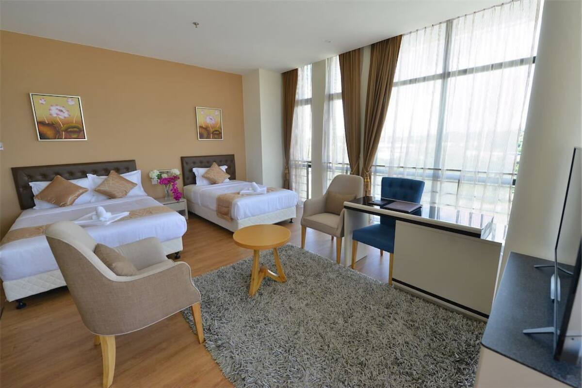 A hotel room with two beds, a desk, a chair, and a TV.