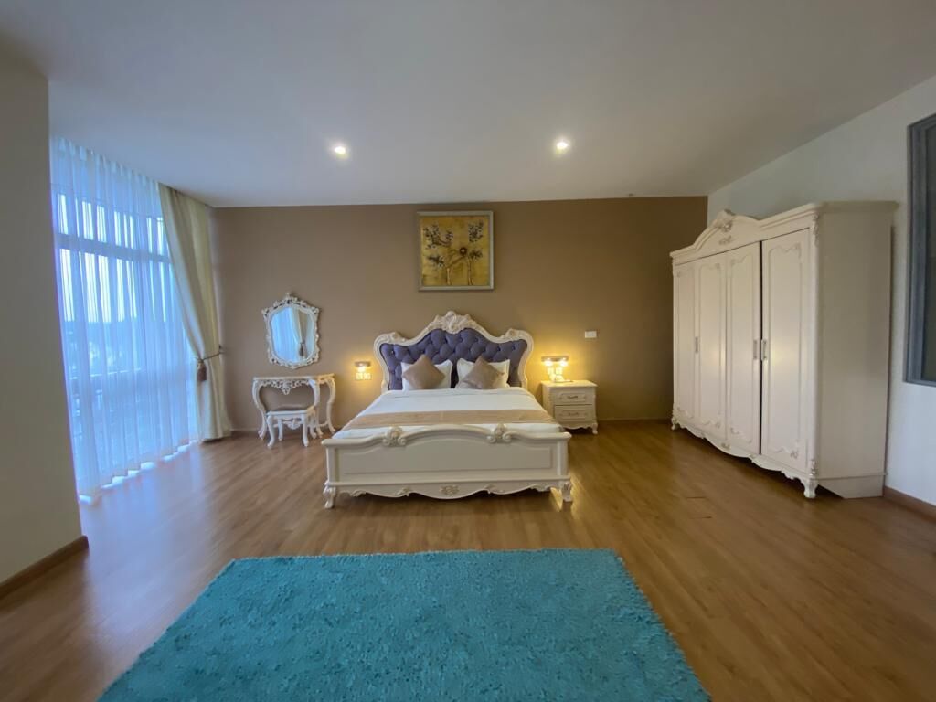 A bedroom with a large bed, a nightstand, a dresser, and a window with curtains.