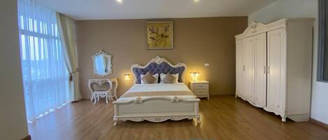 A bedroom with a large bed, a nightstand, a dresser, and a window with curtains.