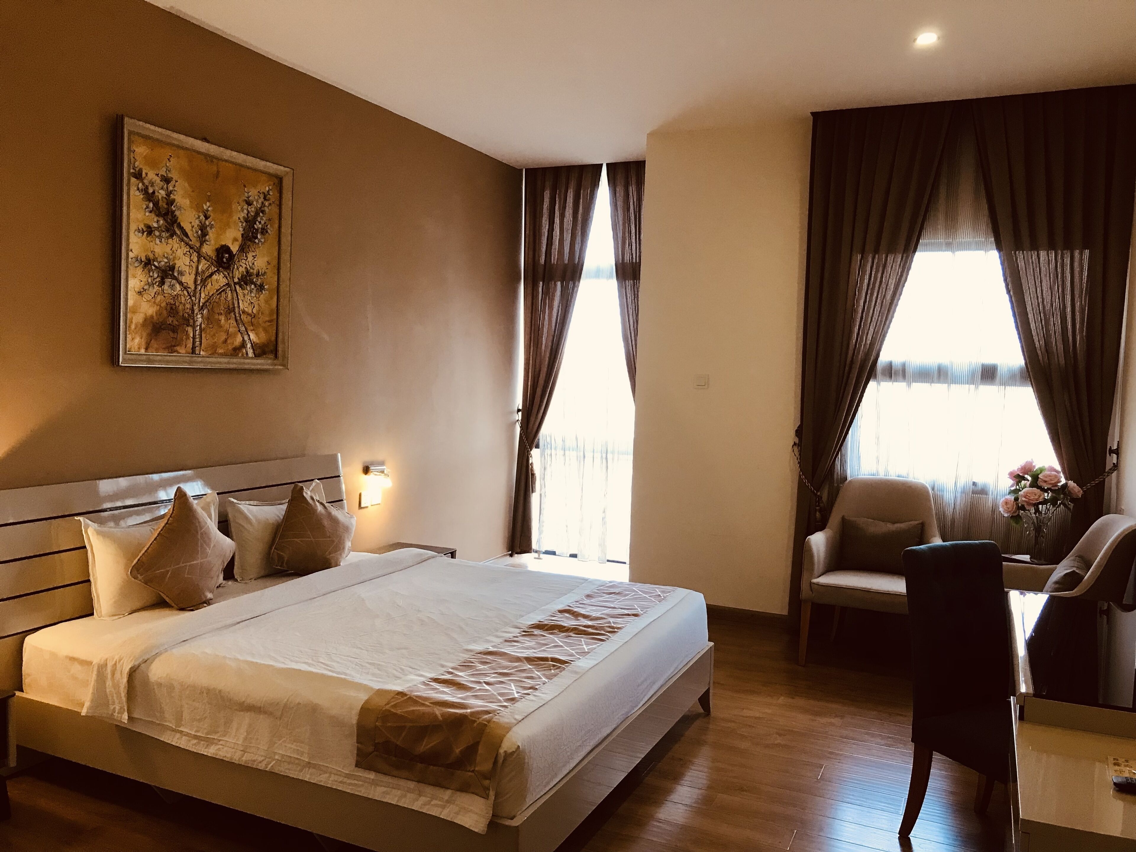 A hotel room with a large bed, a desk, a chair, and a painting on the wall.