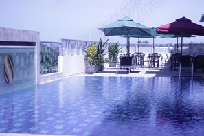 A rooftop pool with clear blue water, surrounded by potted plants and outdoor furniture under umbrellas. - Wafa Hotel & Apartment (Bandar Seri Begawan)