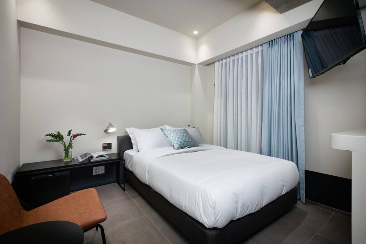 A modern hotel room with a single bed, a desk, and a chair.
