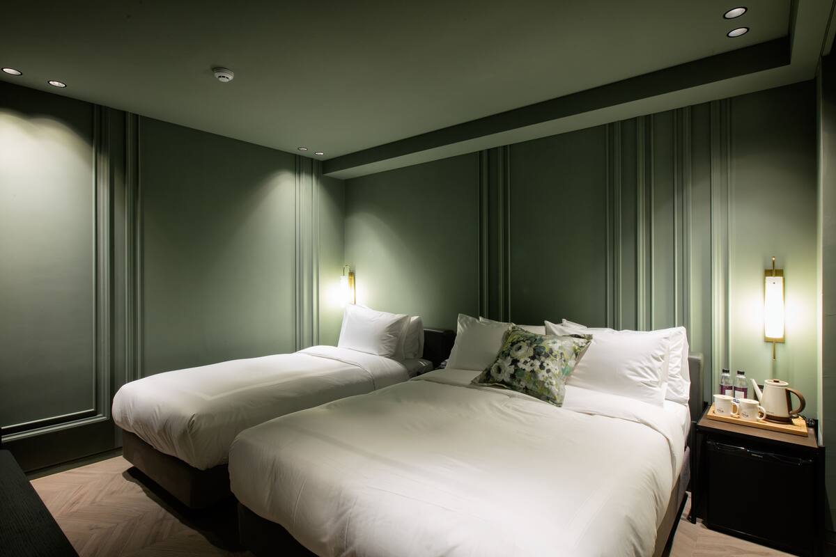 A hotel room with two beds, a nightstand with a coffee maker, and a view of the city.